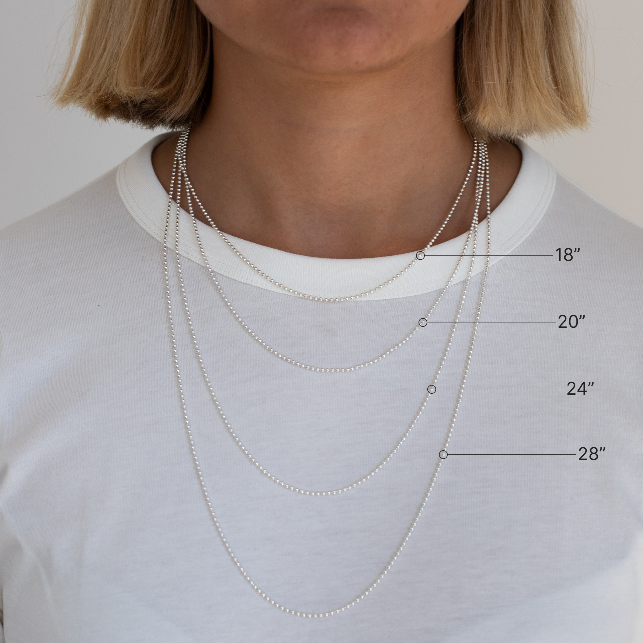 Woman wearing four different length necklaces with measurements indicated on a plain background