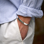 Close-up of a person wearing a silver bracelet with rolled-up sleeves and white trousers.