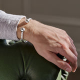 Close-up of a person's wrist wearing silver torque bracelet resting on the end of a sofa