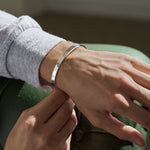 Close-up of a person wearing a silver hammered bracelet resting arm on green sofa