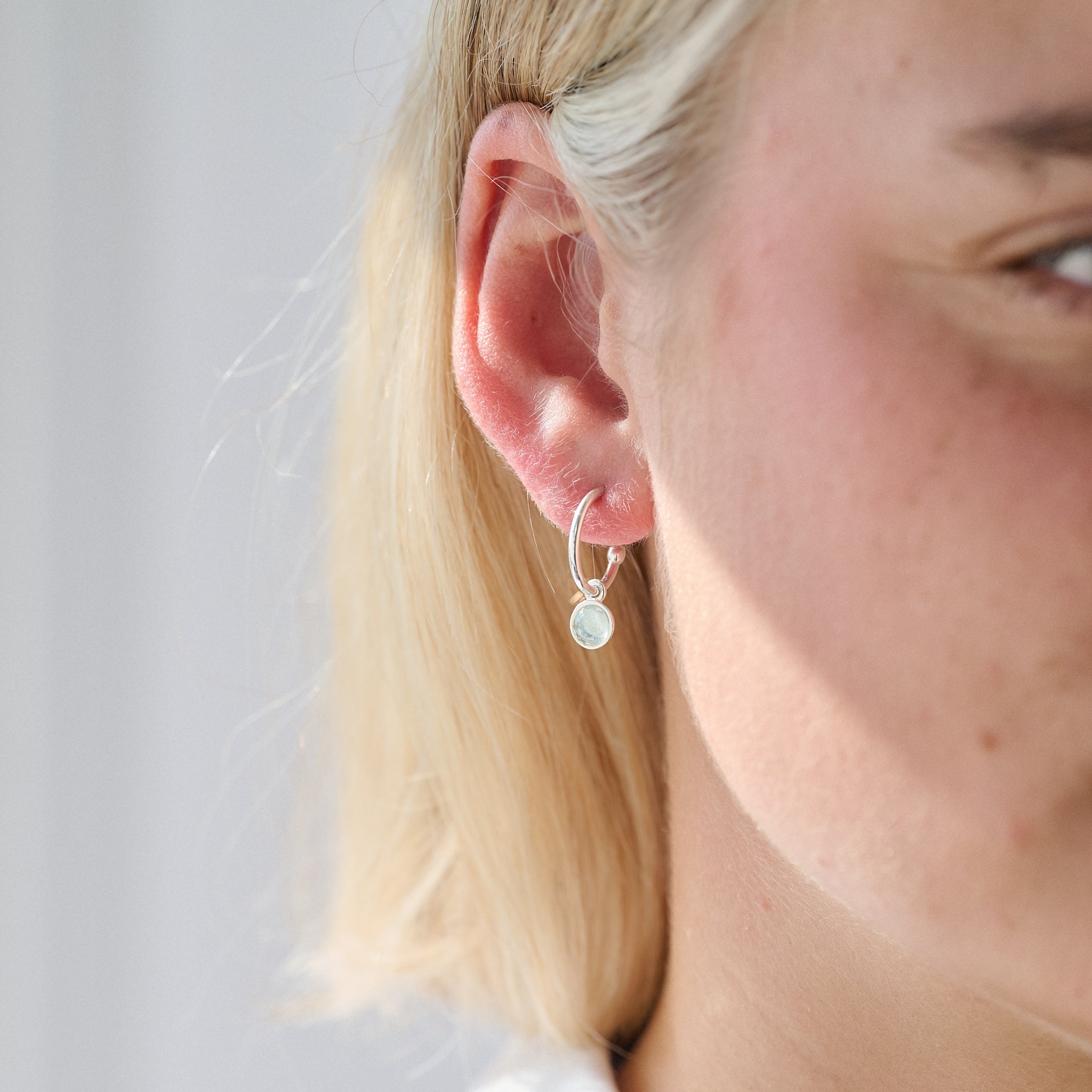 Close-up of a person wearing a silver birthstone hoop earring with a small round gemstone.
