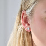Close-up of a person wearing a silver birthstone stud earring with a blurred background