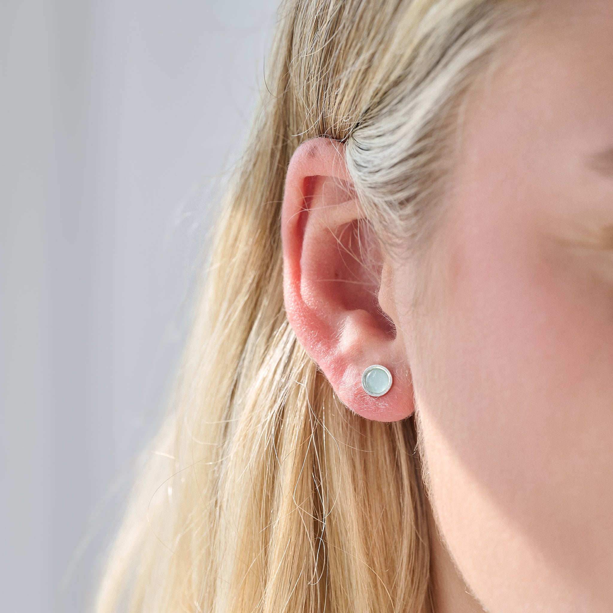 Close-up of a person wearing a silver birthstone stud earring with a blurred background