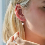 Close-up of a person wearing a silver ball drop earring with a blurred background