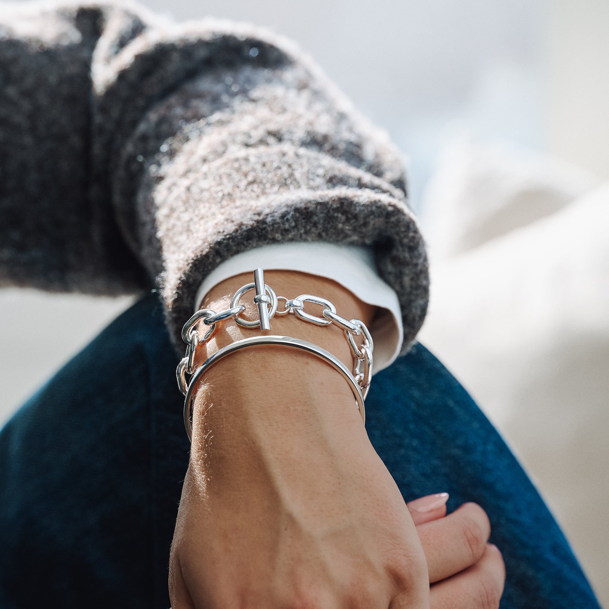 Close-up of a wrist wearing a silver chain bracelet and silver bangle with a blurred background