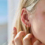 Close-up of a person wearing gold hoop earrings with a blurred background