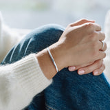 Close-up of a person's wrist with a silver bracelet and white sleeve.