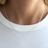 A close-up of a delicate silver chain necklace worn around the neck of a person wearing a white ribbed t-shirt.