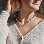 Close-up of a person wearing a silver chain necklace with a neutral background