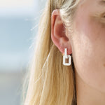 Close-up of a person wearing silver deco drop earrings with a blurred background