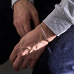 Close-up of a person's wrist wearing a silver bracelet against a dark background