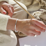 Close-up of a person's hand holding a paint brush wearing a silver bracelet and ring with a blurred background