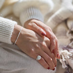 Close-up of a person's hands with a silver ring and bracelet, wearing a white sweater.