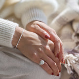 Close-up of a person's hands with a silver ring and bracelet, wearing a white sweater.