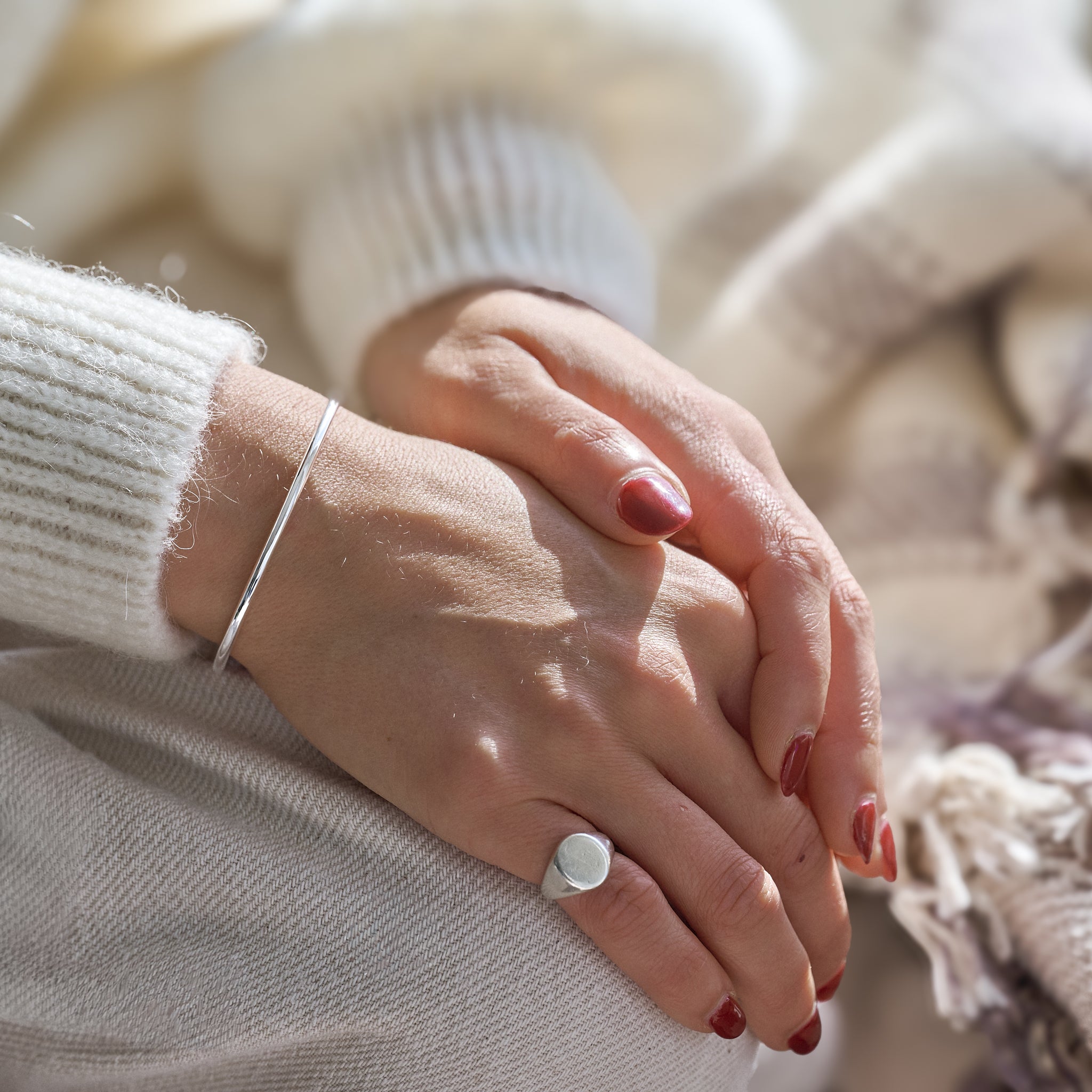 Close-up of a person's hands with a silver ring and bracelet, wearing a white sweater.