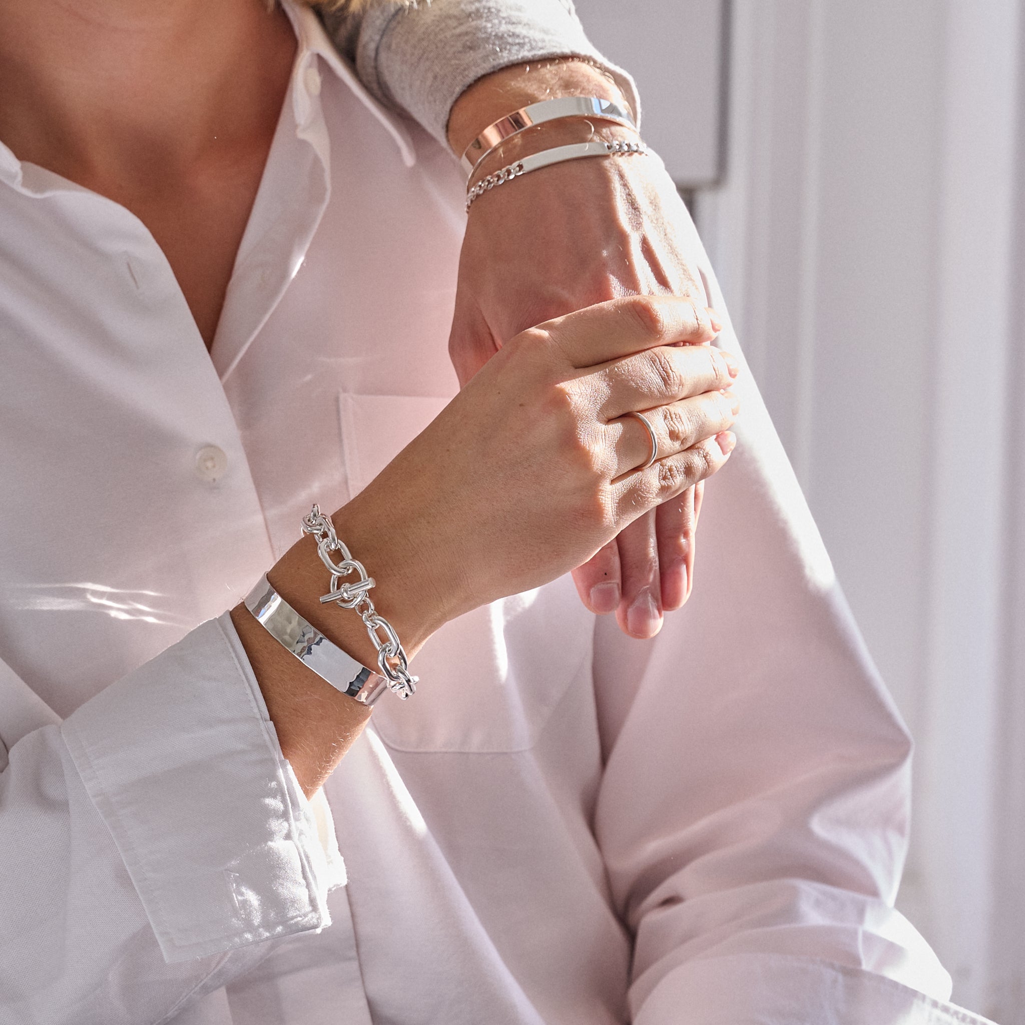 Close-up of hands wearing multiple bracelets and rings, with a blurred background.