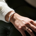 Close-up of a wrist wearing a silver bracelet with a blurred background