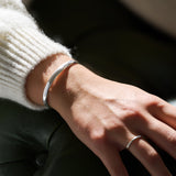 Close-up of a wrist wearing a silver bracelet with a blurred background