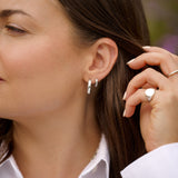 Close-up of a woman adjusting her silver hoop earrings.