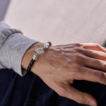 Person wearing a black braided bracelet with a silver t-bar clasp on a neutral background