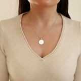 Necklace with a round pendant worn by a person in a beige top.