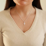 Person wearing a silver cross necklace against a neutral background
