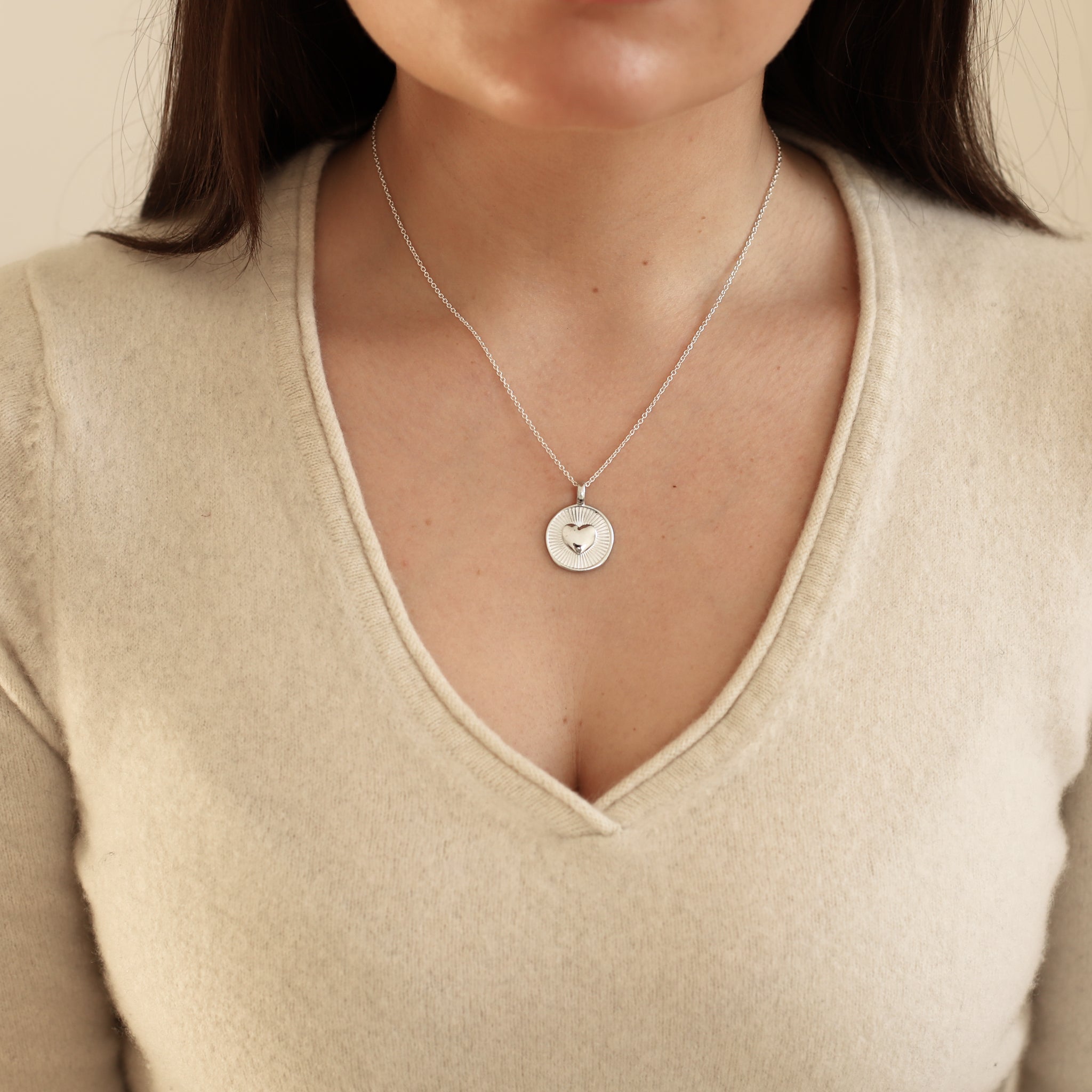 Necklace with a circular pendant worn by a person in a beige sweater.