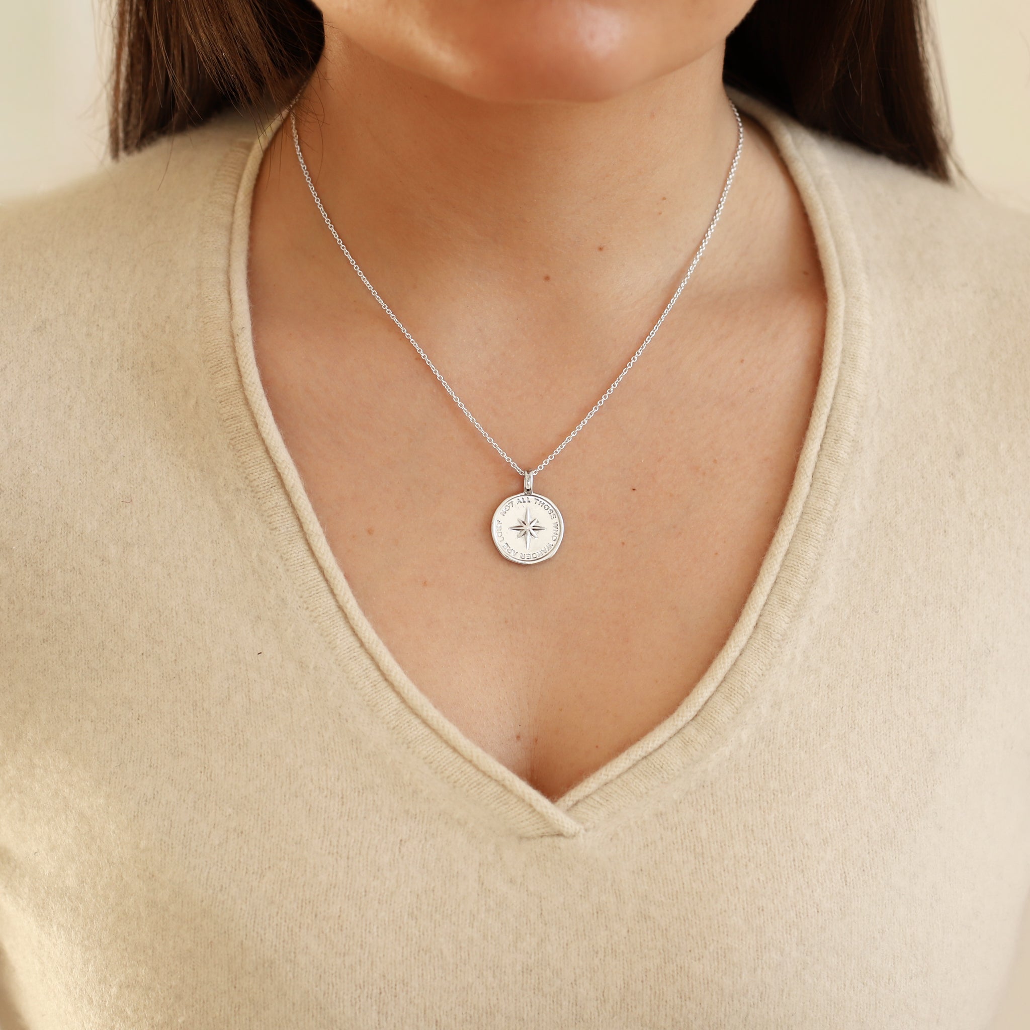Silver necklace with a round pendant worn by a person in a beige top.