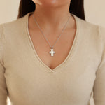 Silver cross necklace worn by a person in a beige sweater
