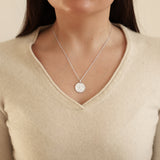 Silver necklace with a pendant worn by a person in a beige sweater.