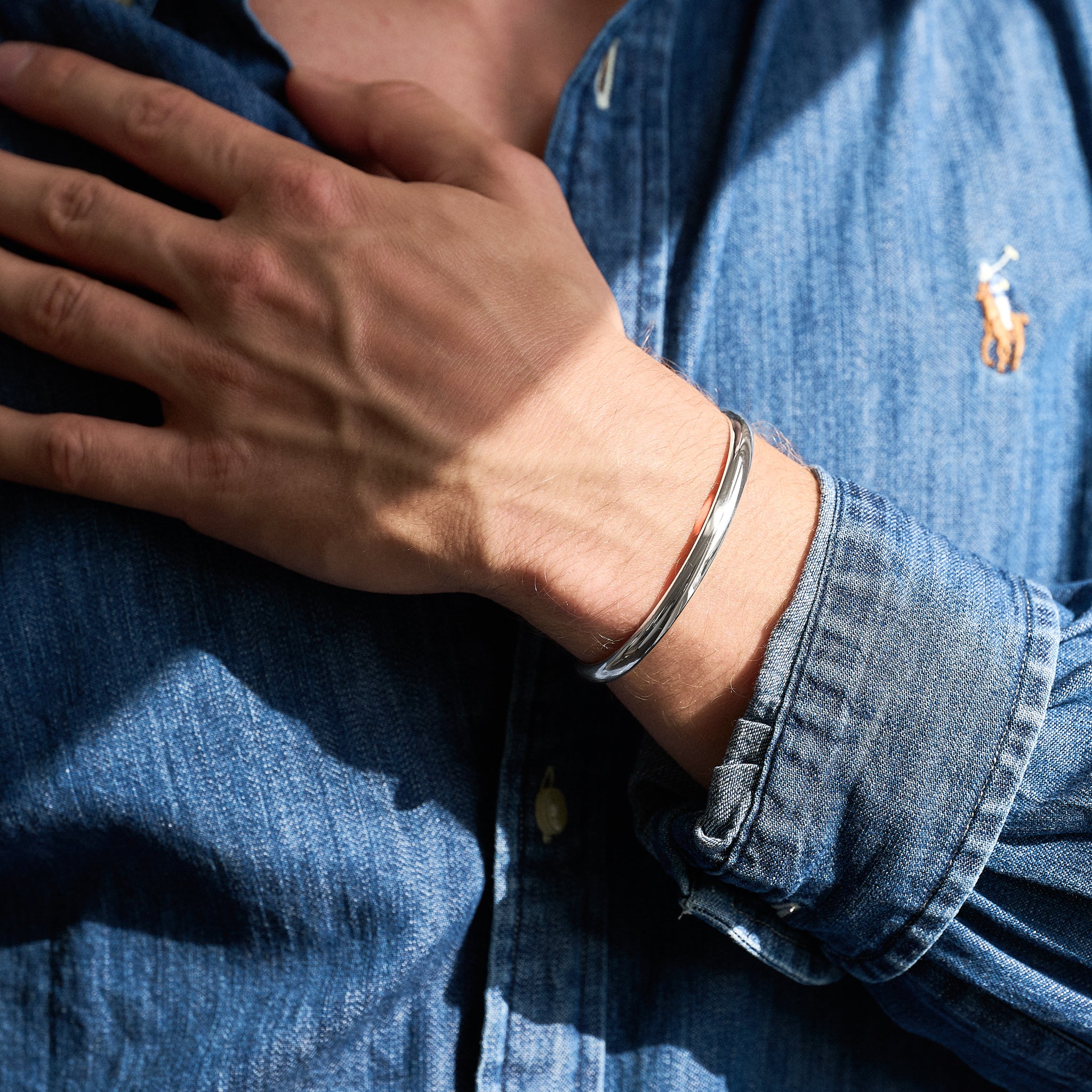 Person wearing a silver bracelet on a blue denim shirt background
