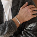 Person wearing a silver beaded bracelet on a grey jacket