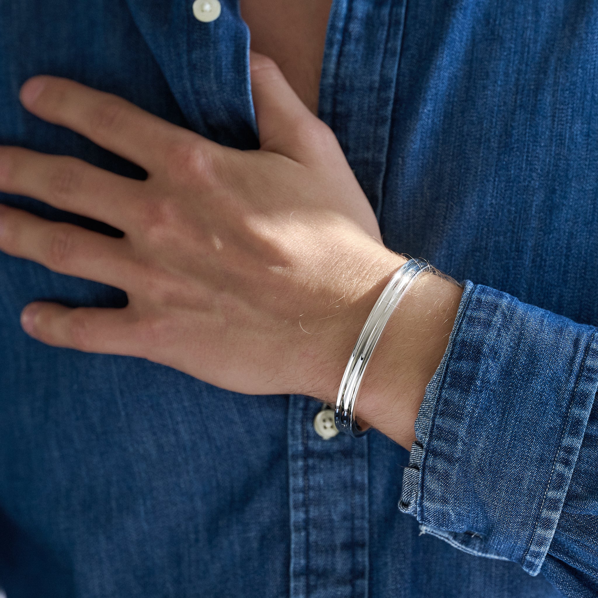 Person wearing a silver ribbed bracelet on a blue denim shirt