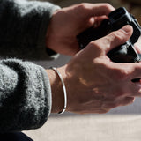 Close-up of hands holding a camera with silver bracelet on wrist and a blurred background