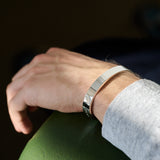 Hand wearing a silver bracelet on a dark background