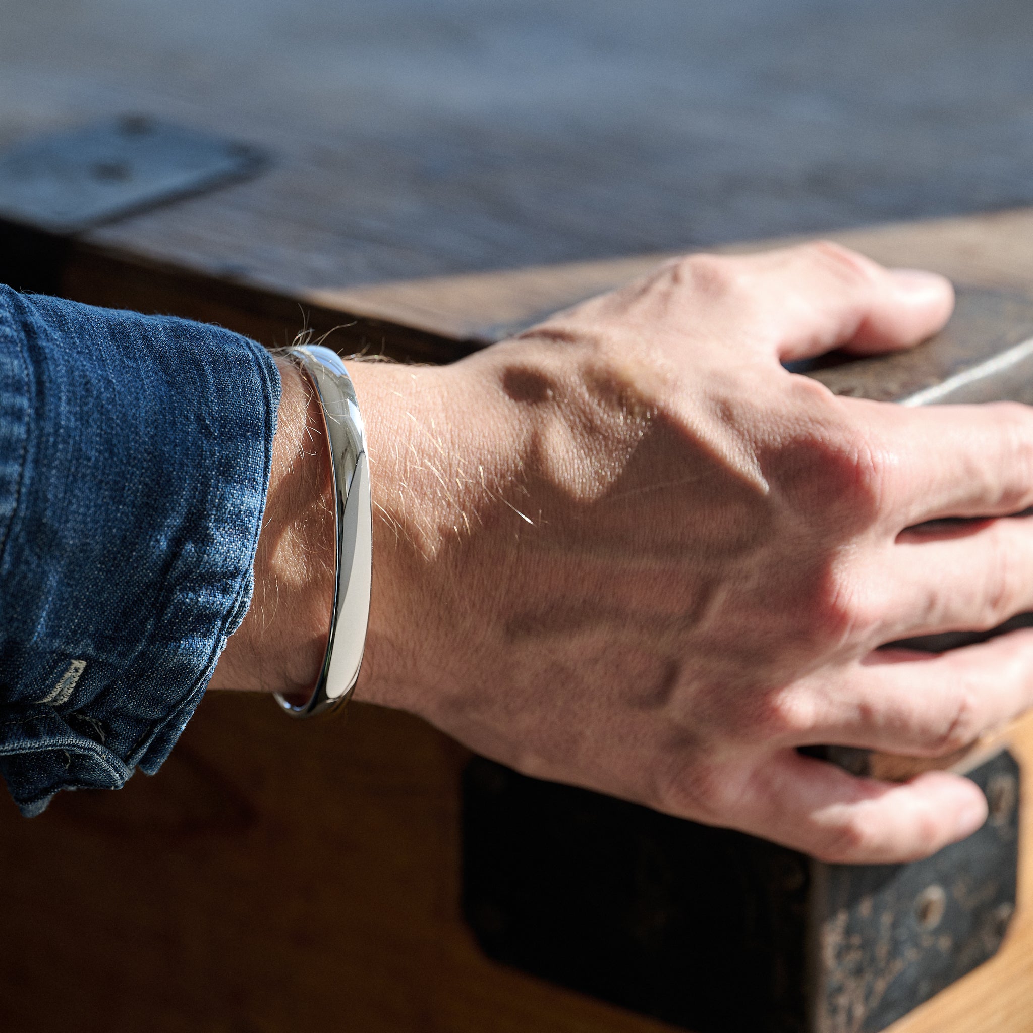 Person wearing a silver bracelet holding a wooden box on a blurred background