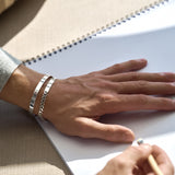Hand on a light surface with silver chain bracelet and silver cuff bracelet on wrist