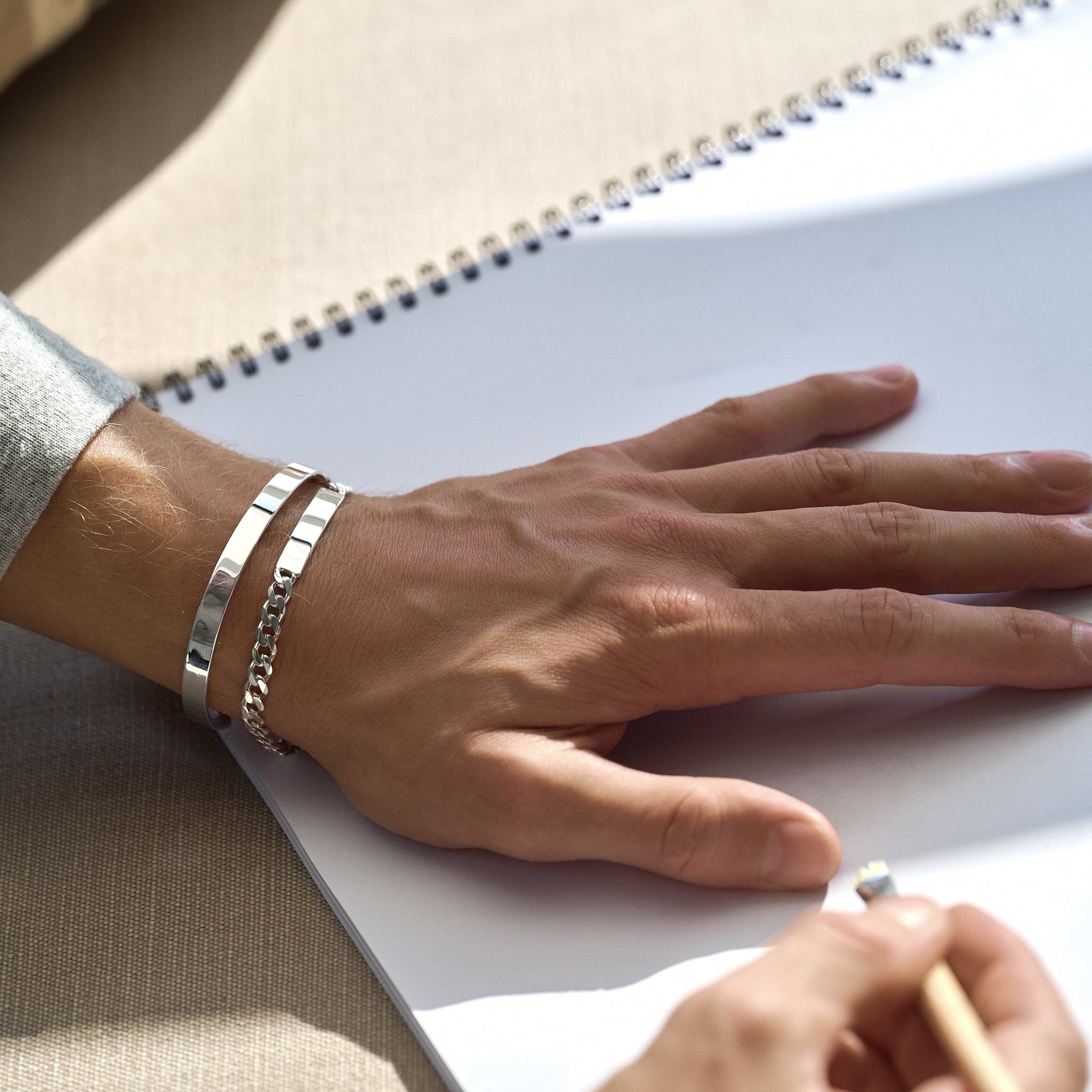 Hand on a light surface with silver chain bracelet and silver cuff bracelet on wrist