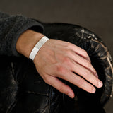 Hand wearing a silver bracelet on a dark background