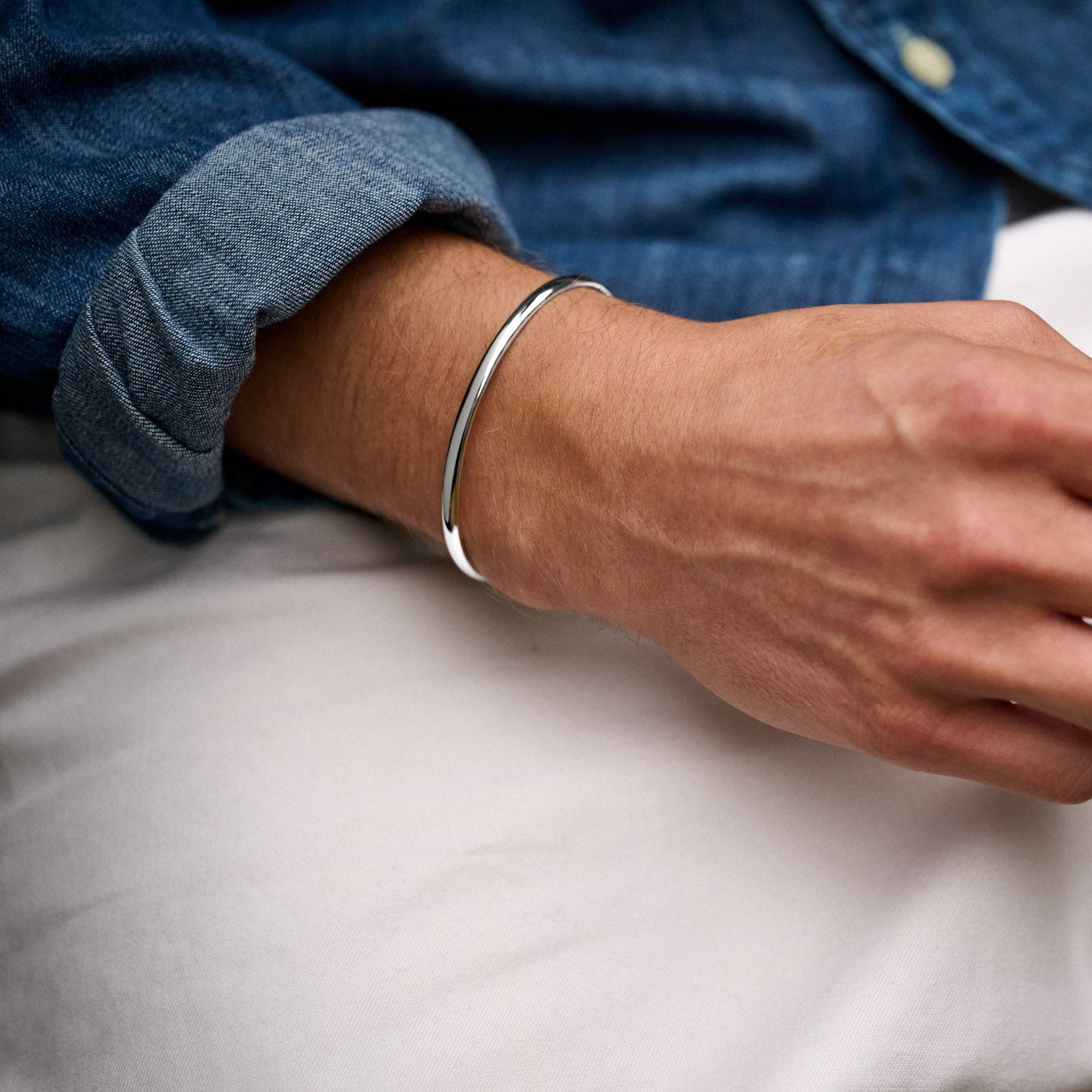Close-up of a person's wrist wearing a silver bracelet with a blue shirt and white fabric background.