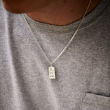 Person wearing a grey shirt with a necklace featuring a rectangular pendant.