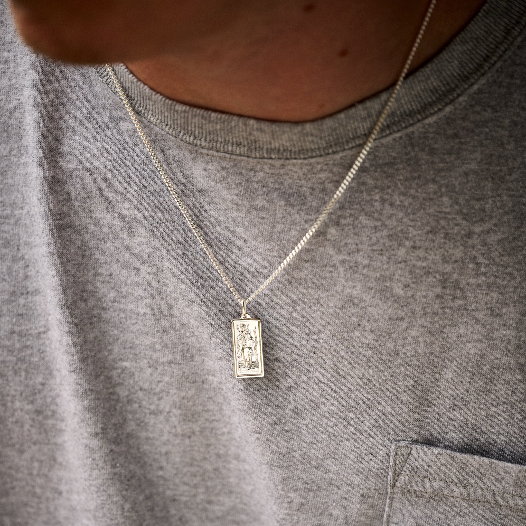 Person wearing a grey shirt with a necklace featuring a rectangular pendant.