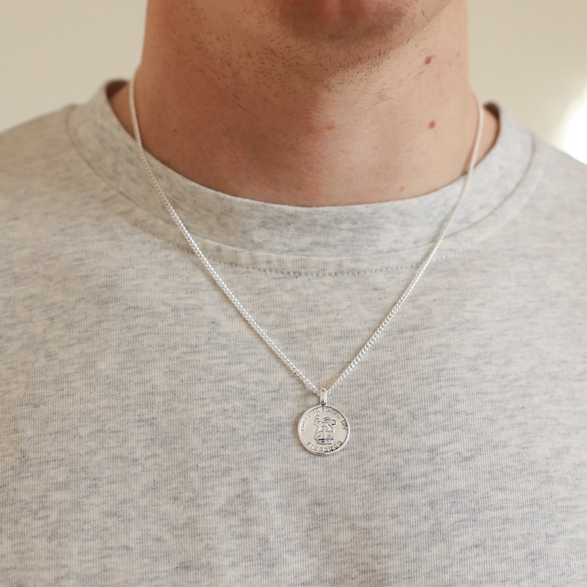 Person wearing a silver necklace with a round pendant on a plain background