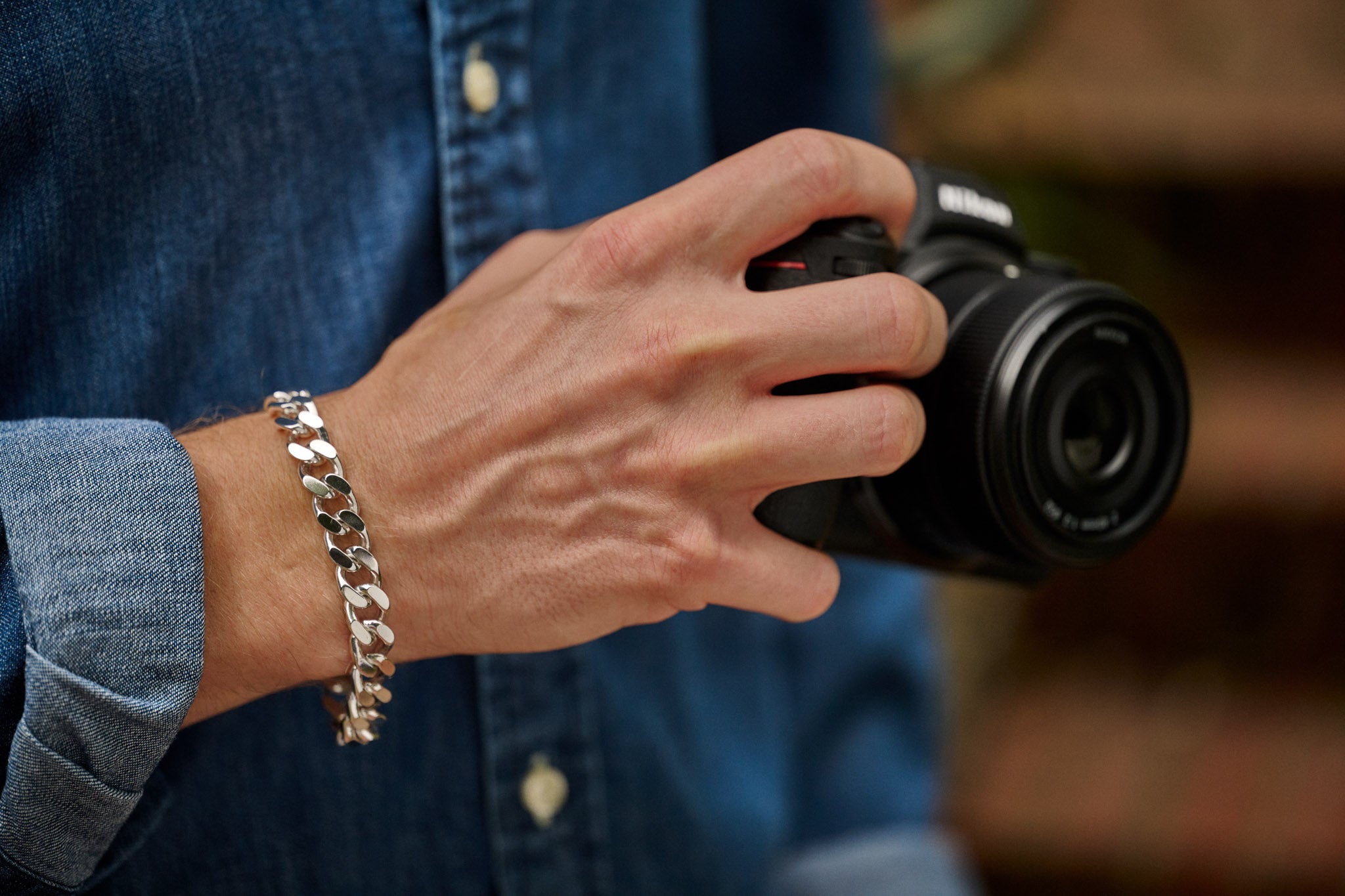 Hand holding a camera with a blurred background and silver bracelet on wrist
