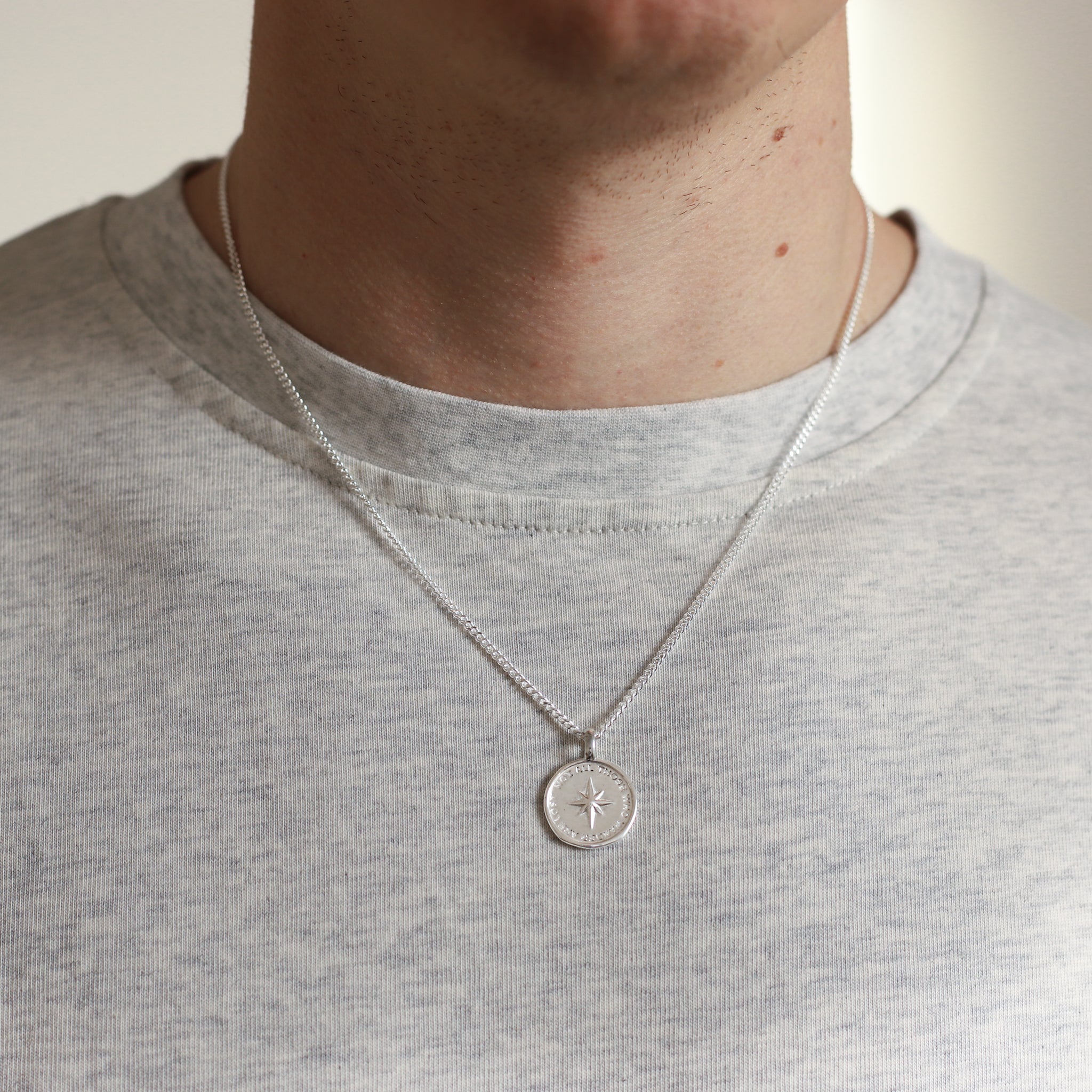 Person wearing a silver necklace with a round pendant on a plain background