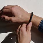 Close-up of a hand adjusting a black braided bracelet on another wrist.