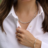 Person wearing a silver chain necklace, ring, and bracelet on a white shirt.
