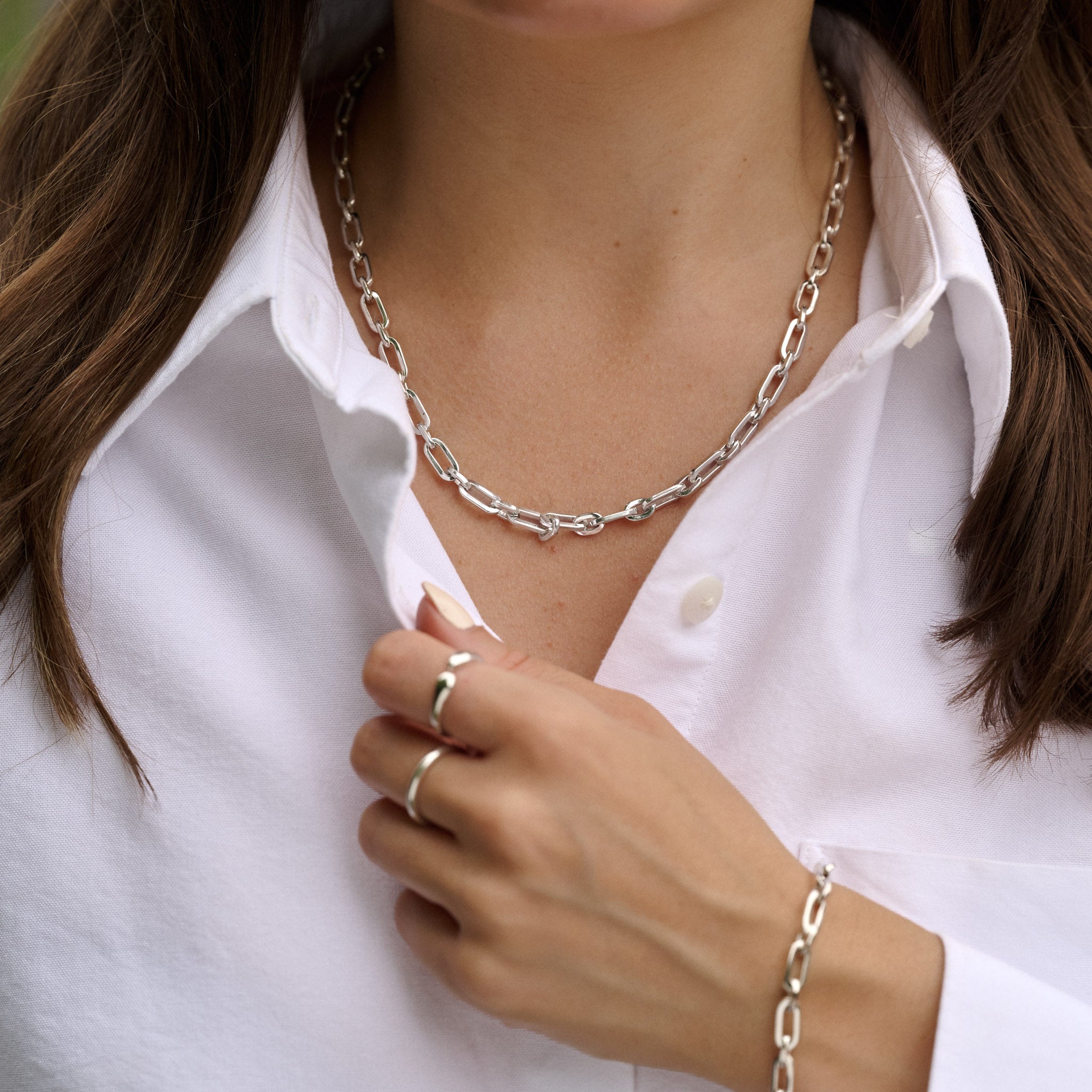 Person wearing a silver chain necklace, ring, and bracelet on a white shirt.