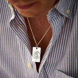 Person wearing a necklace with a silver pendant on a blue and white striped shirt.