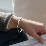 Person wearing a hammered silver bracelet on a neutral background